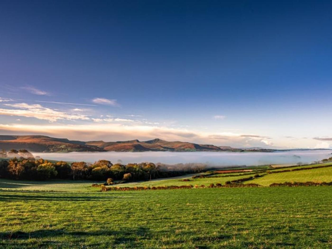 Ein weiter Blick über ein grünes Feld mit einem See und Bergen in der Ferne.