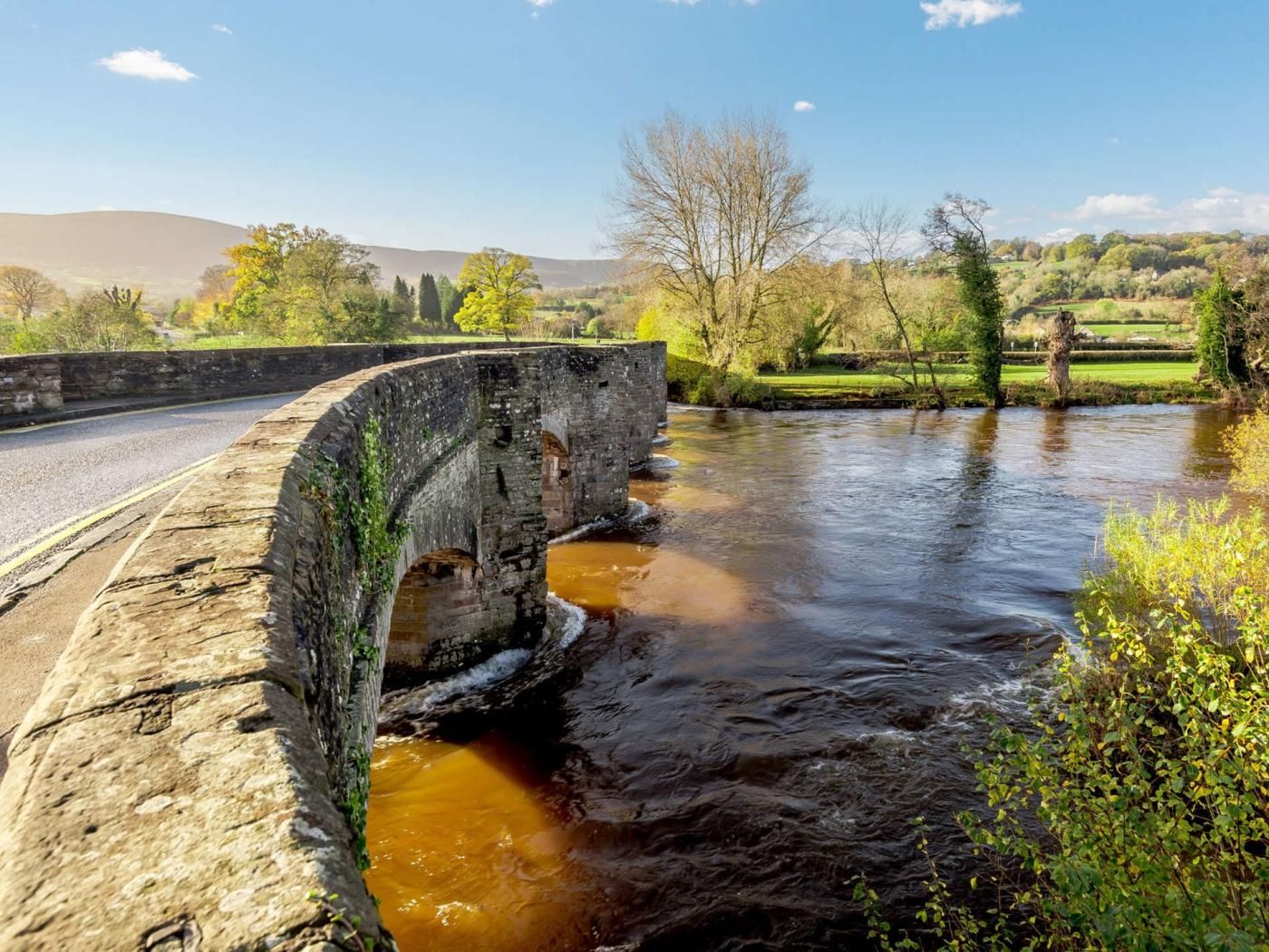 A stone bridge over a river with a road on the left.