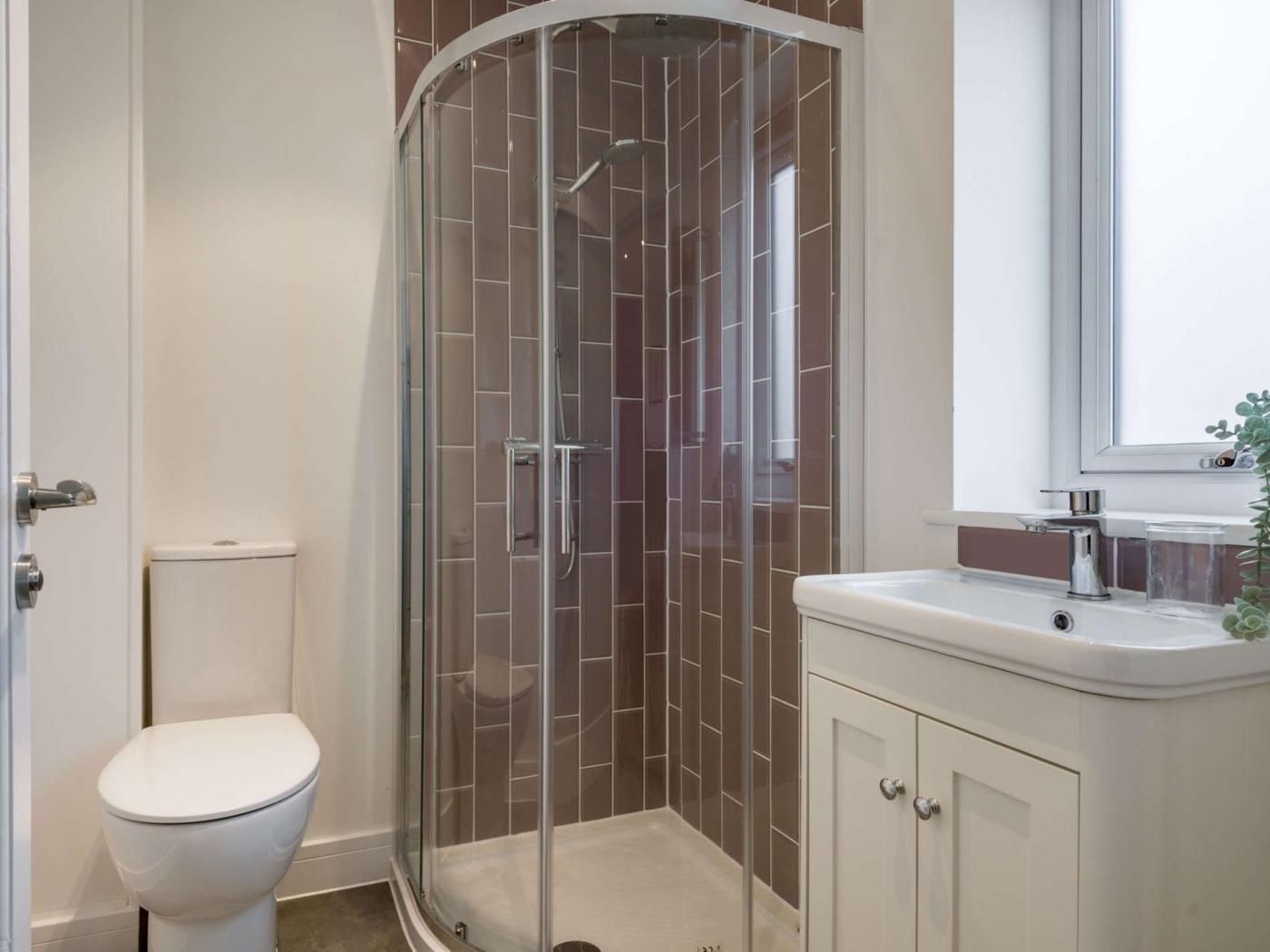 A bathroom with a glass-enclosed shower, a toilet, and a sink with a mirror above it.