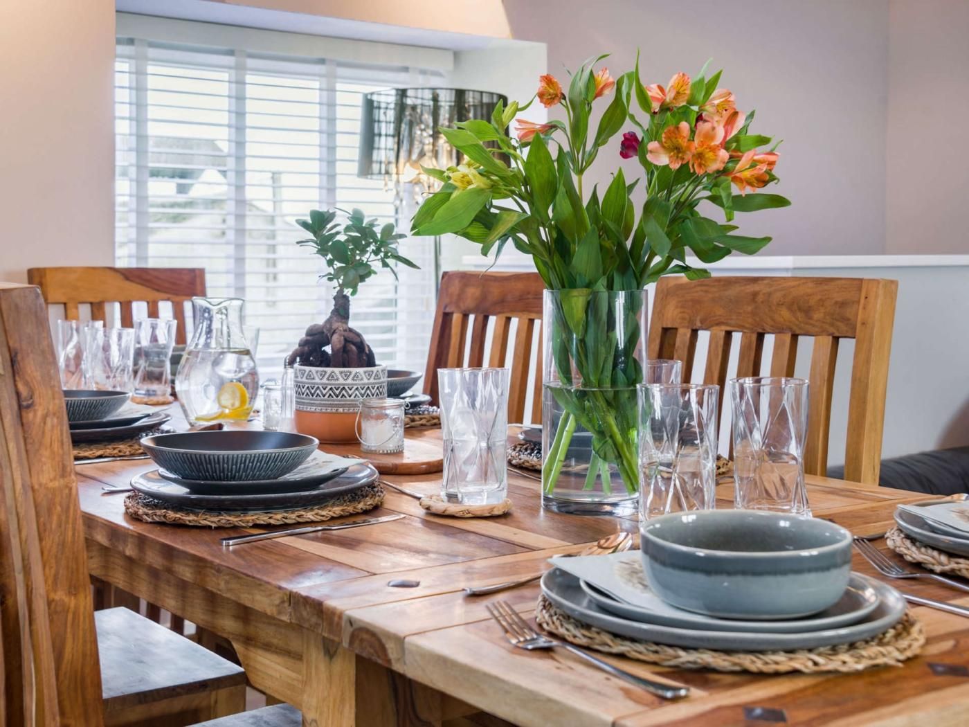 A dining table set with plates, bowls, glasses, and a vase with flowers.