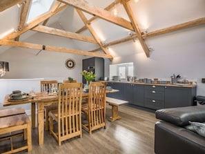 A loft-style room with exposed wooden beams, a dining area with wooden furniture, a kitchen with dark cabinets, and a leather sofa. - 4 Bed in Axbridge (oc-90365) (Biddisham)