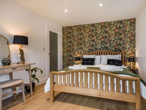 A bedroom with a wooden bed, a desk with a lamp, and a floral wallpaper. - 4 Bed in Axbridge (oc-90365) (Biddisham)