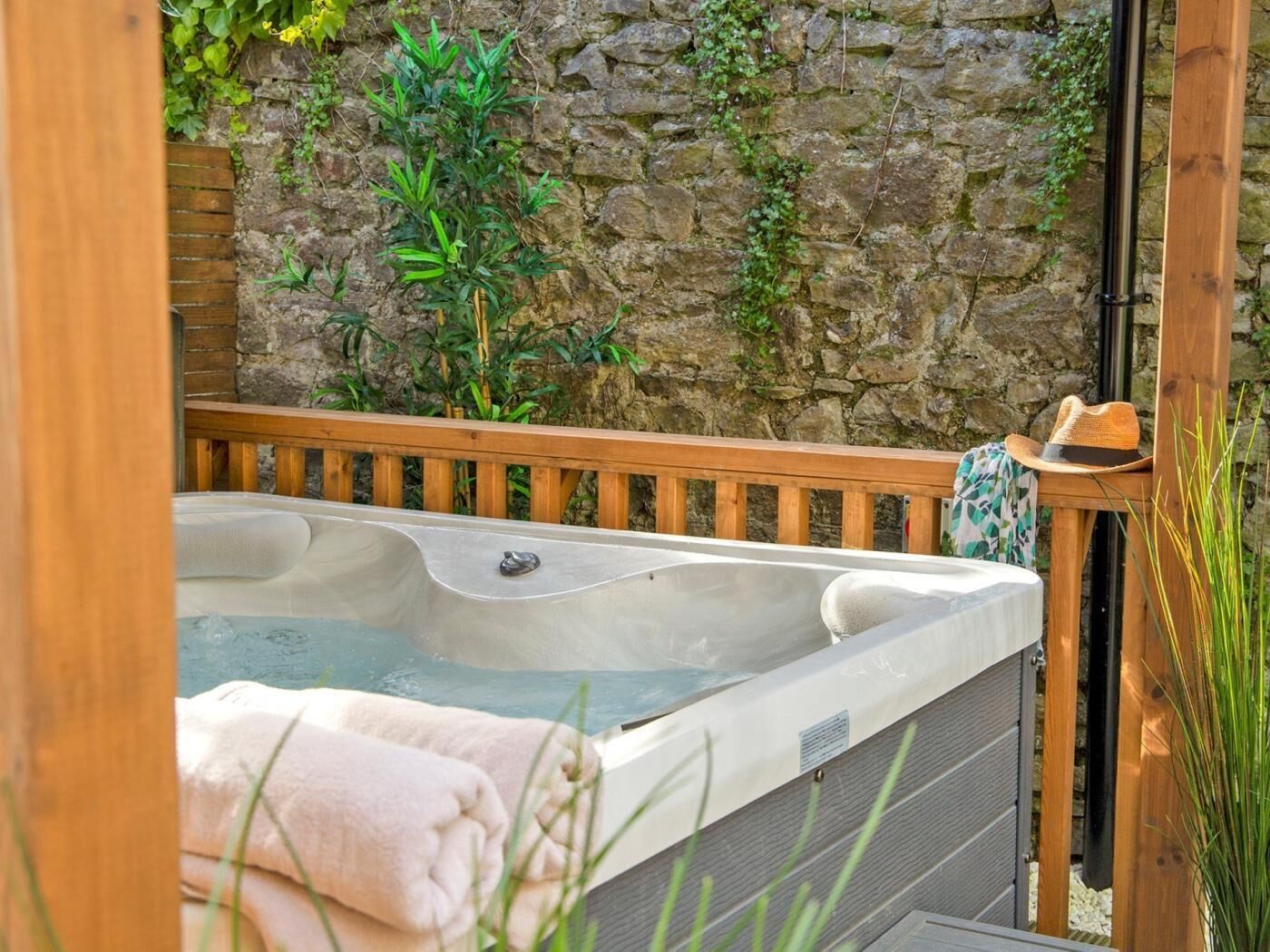 A hot tub in a wooden deck area with a stone wall backdrop and a hat on a wooden post.