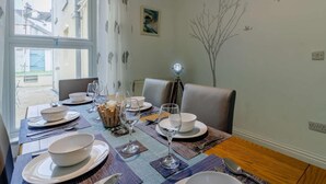 Un coin repas avec une table dressée pour quatre personnes, une fenêtre avec des rideaux, un luminaire fixé au mur et un motif décoratif représentant un arbre.