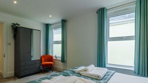 Une chambre à coucher avec un lit, deux serviettes, une chaise, une armoire et une fenêtre avec des rideaux.