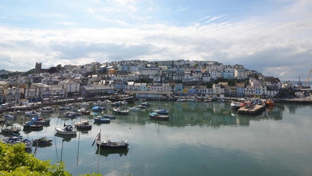 Une ville côtière dotée d’un port de plaisance rempli de bateaux, de bâtiments historiques et d’une église située sur une colline.