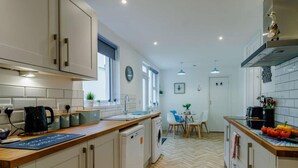 Une cuisine moderne avec des meubles blancs, un plan de travail en bois, un lave-vaisselle et un coin repas comprenant une table et des chaises.