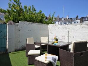 Un patio con mobiliario de mimbre, una mesa y una botella de vino.
