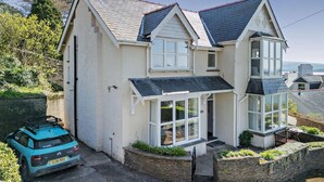 A two-story house with a prominent bay window, a conservatory, and a car parked in the driveway. - 5 Bed in Aberdovey (oc-90493) (Aberdovey)