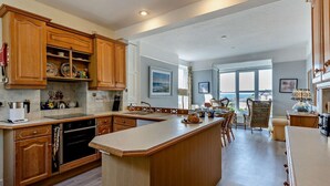 A spacious kitchen with wooden cabinets, a central island, and a dining area with chairs. - 5 Bed in Aberdovey (oc-90493) (Aberdovey)