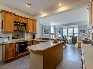 A spacious kitchen with wooden cabinets, a central island, and a view to the outside. - 5 Bed in Aberdovey (oc-90493) (Aberdovey)