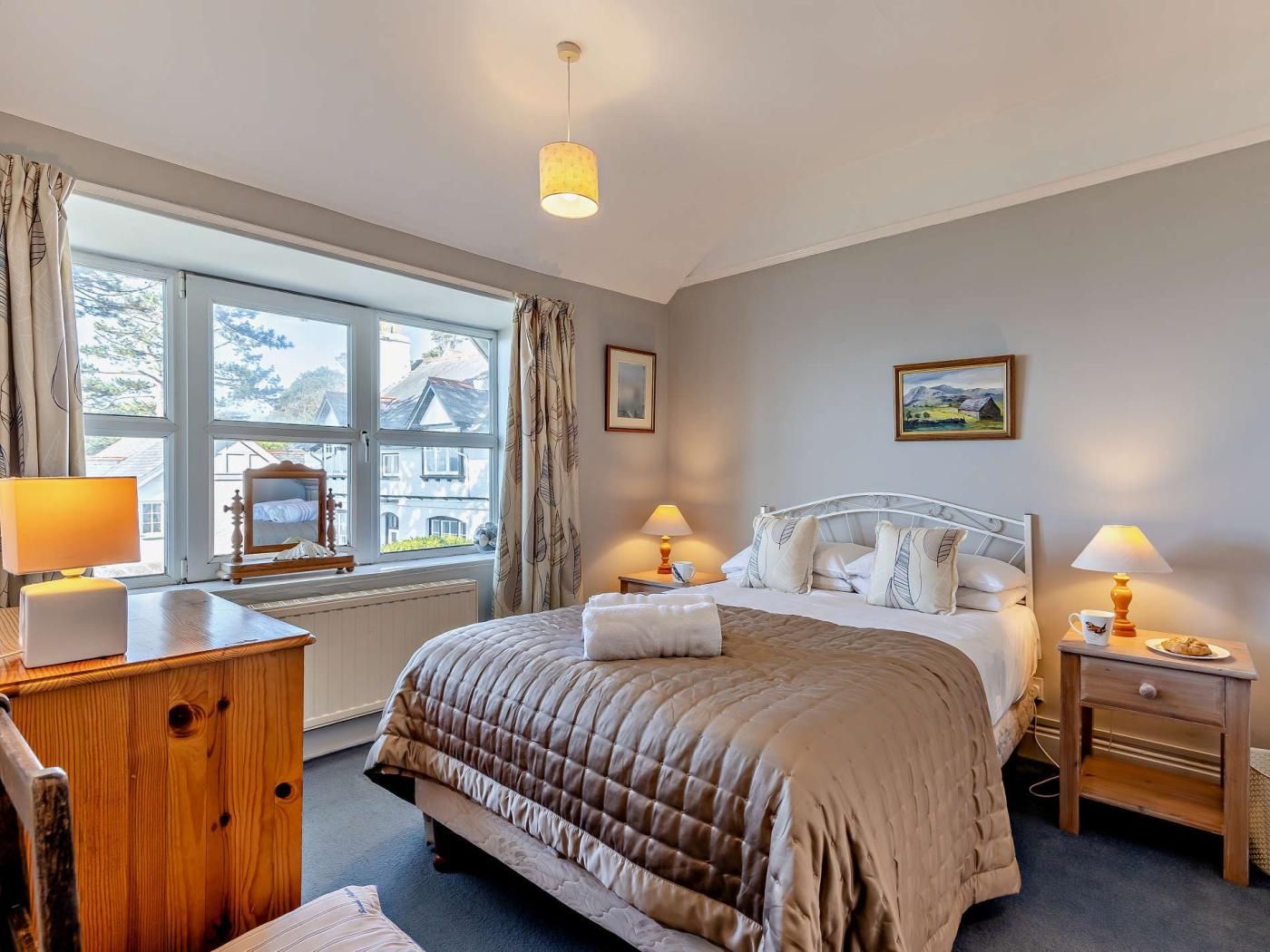 Ett hotellrum med en stor säng, sänglampor, en byrå i trä och ett fönster med gardiner.