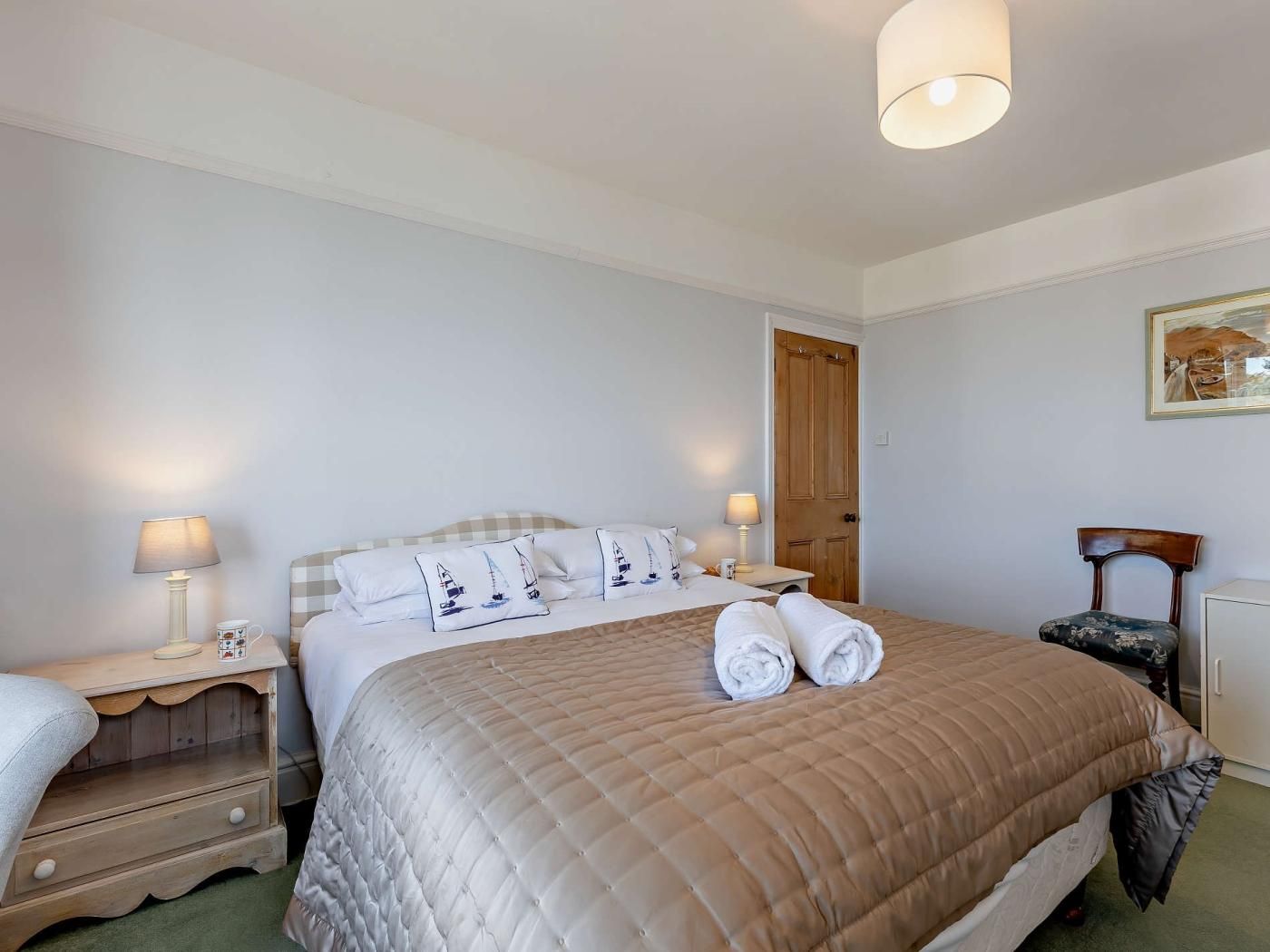 Une chambre d’hôtel avec un lit, deux tables de chevet, une chaise, un bureau et une porte.