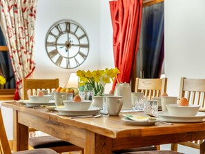 Ein Holztisch ist gedeckt mit Tellern, Schüsseln, Tassen und einer Vase mit gelben Blumen.