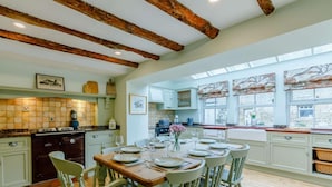 A kitchen with wooden beams, a dining table set for four, and a view through large windows. - 4 Bed in Hexham (oc-90521) (Bardon Mill)