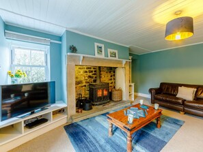 A living room with a stone fireplace, a television, a brown leather sofa, and a coffee table.