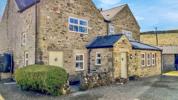 A stone building with multiple windows and doors, a small attached structure, and a well-maintained hedge. - 4 Bed in Hexham (oc-90521) (Bardon Mill)