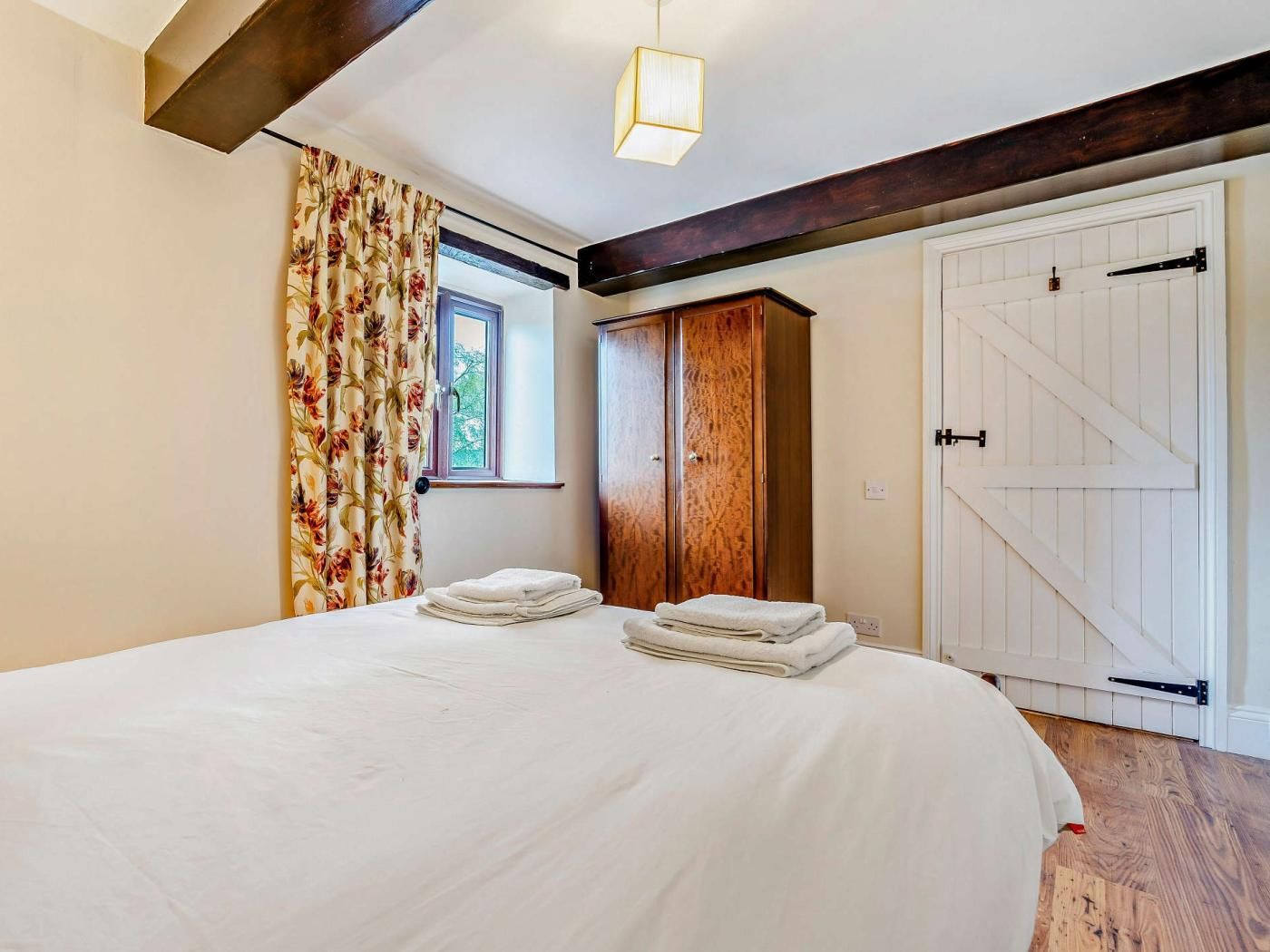 A bedroom with a large bed, a wardrobe, a window with curtains, and a door with a barn-style design.