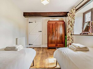 Een kamer met twee bedden, een houten garderobe, een radiator en een raam met gordijnen.