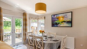 Un coin repas avec une table dressée pour quatre personnes, une grande fenêtre donnant sur un paysage verdoyant et un tableau accroché au mur.