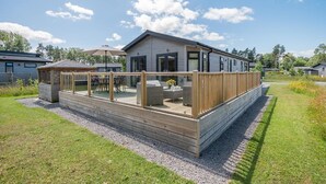 Une maison moderne dotée d’une terrasse, d’un espace salon extérieur abrité et d’un petit jardin.