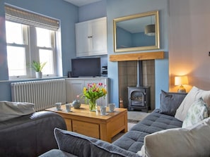A living room with a sofa, a coffee table with cups and a vase of flowers, a television, a fireplace, and a mirror on the wall. - 3 Bed in Bakewell (oc-90384) (Bakewell)