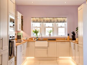 A modern kitchen with white cabinets, a central island, a window with a floral valance, and a sink. - 3 Bed in Bakewell (oc-90384) (Bakewell)