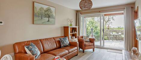A living room with a brown leather sofa, a wooden side table, a white chair, and a dining area with a table and chairs.
