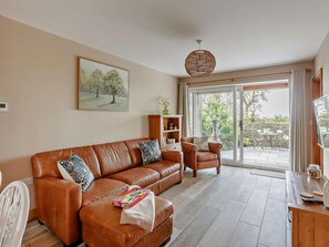 Una sala de estar con un sofá de cuero marrón, una mesita de madera, una silla blanca y un comedor con mesa y sillas.