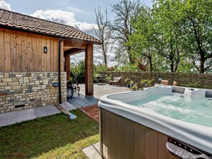 Un jacuzzi en un patio trasero con una casa de madera y un muro de piedra.