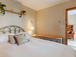 Quarto com cama, mesa de cabeceira, abajur e um banco de madeira.