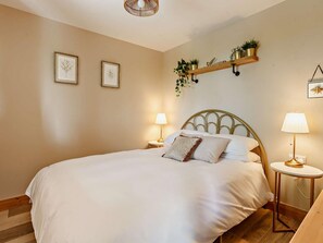 Un dormitorio con una cama, dos lámparas de noche, un estante en la pared con plantas y dos cuadros enmarcados.