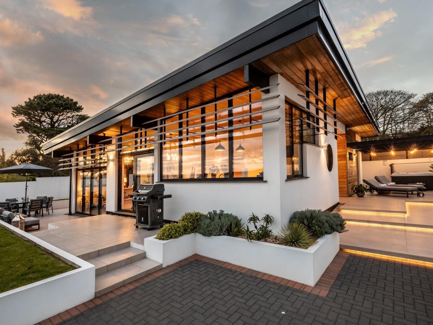 A modern house with a patio, outdoor seating, and a barbecue grill.