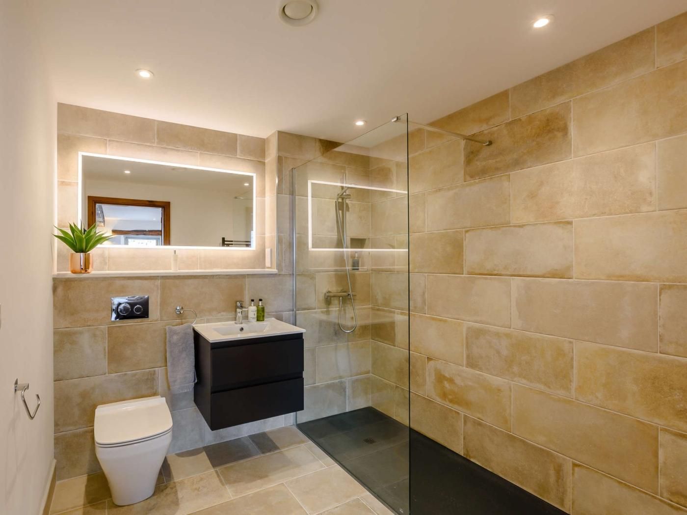 A modern bathroom with a glass-enclosed shower, a white toilet, and a black vanity with a mirror above it.