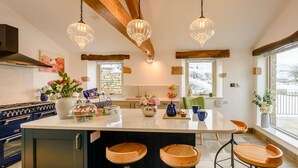 A kitchen with a central island, wooden stools, pendant lights, and a stone wall. - 5 Bed in Lancaster (oc-90546) (Bentham)