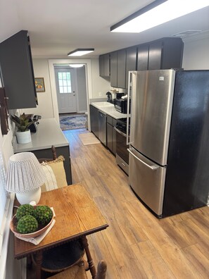 A modern kitchen with stainless steel appliances, a dining area with a wooden table, and a view of the adjacent living room.
