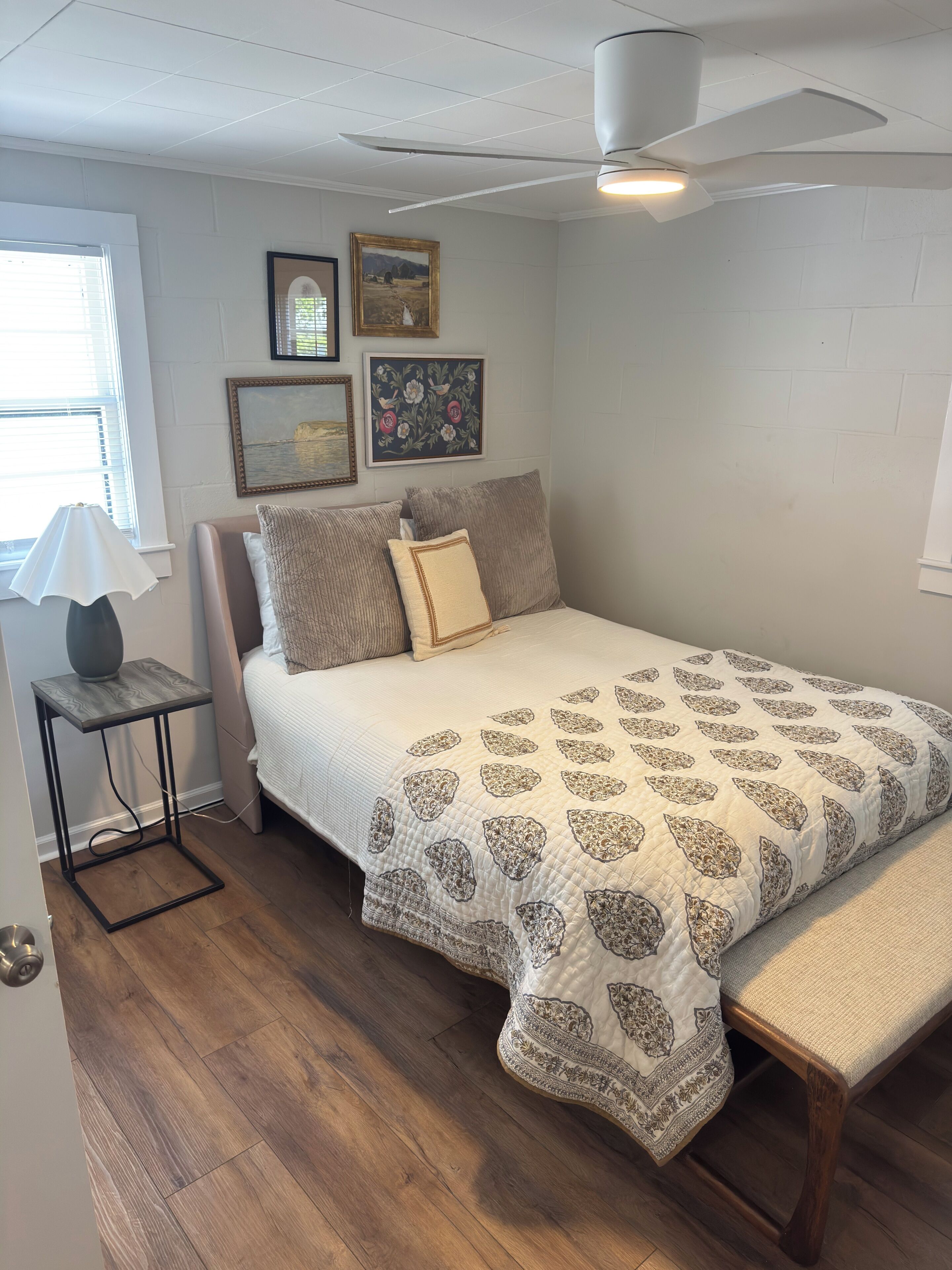 Een slaapkamer met een bed, nachtkastje, plafondventilator en wanddecoratie.