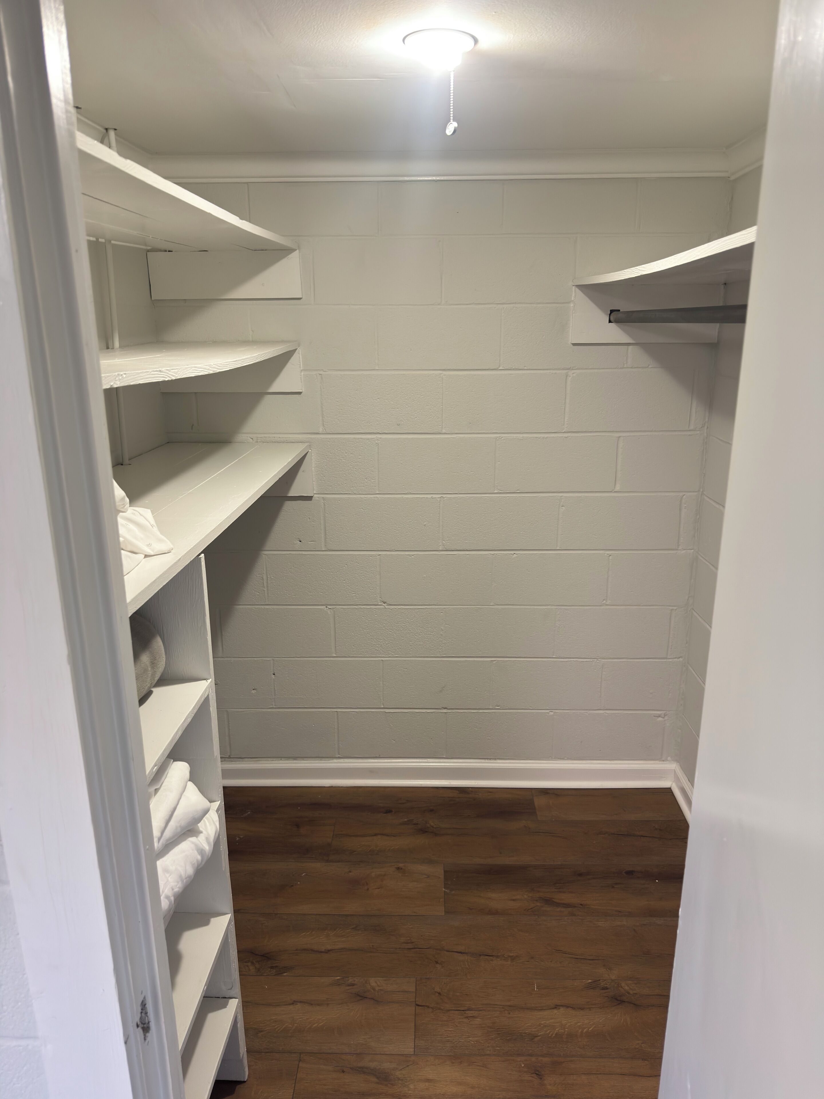 A walk-in closet with white shelving, a wooden floor, and a white wall.