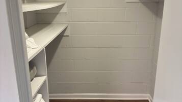 A walk-in closet with white shelving, a wooden floor, and a white wall.