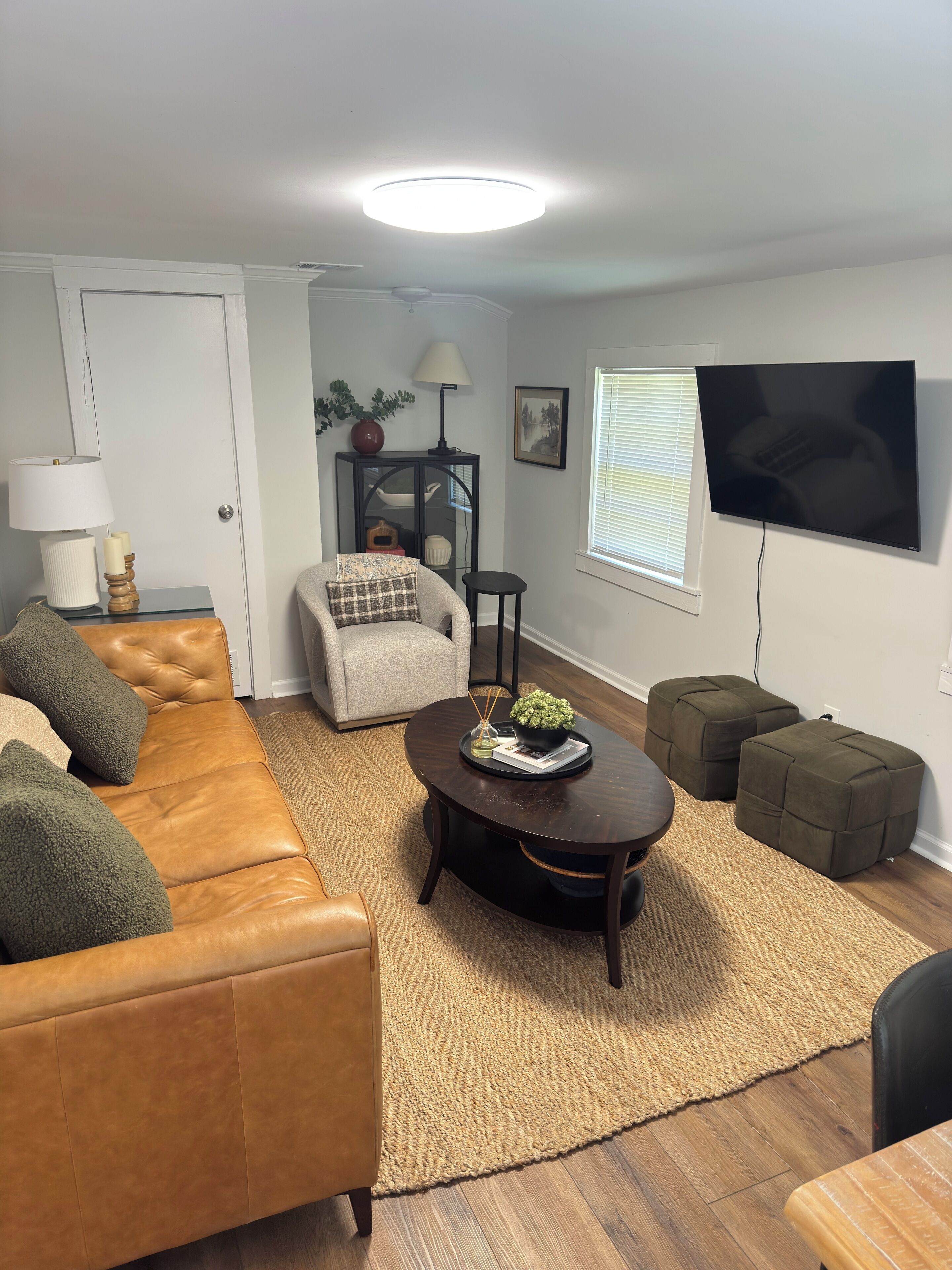 A living room with a sofa, ottomans, a coffee table, a TV, and a lamp.
