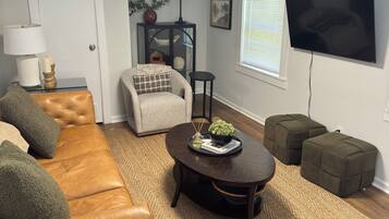A living room with a sofa, ottomans, a coffee table, a TV, and a lamp.