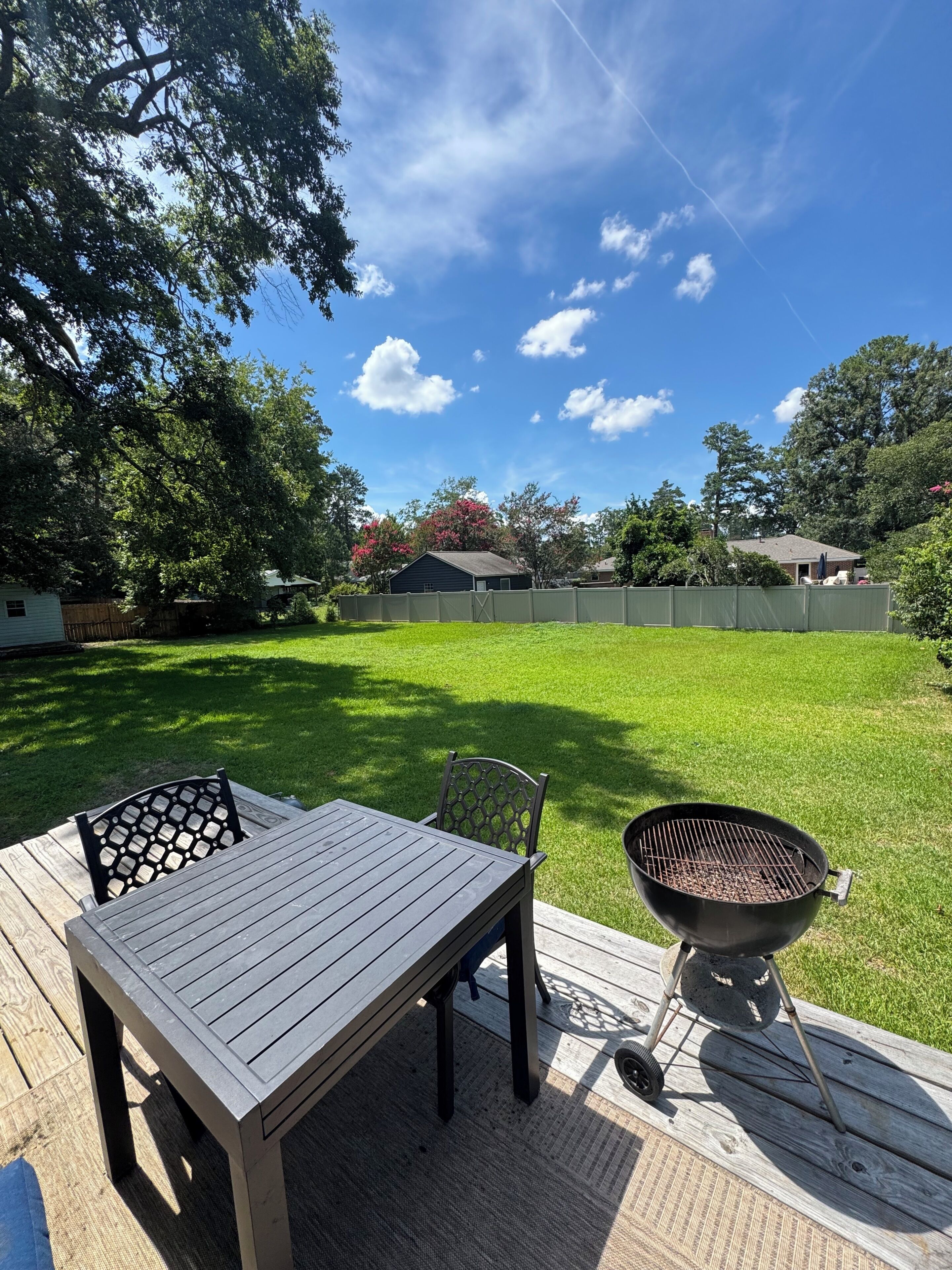A backyard with a wooden deck, a table with chairs, and a grill.