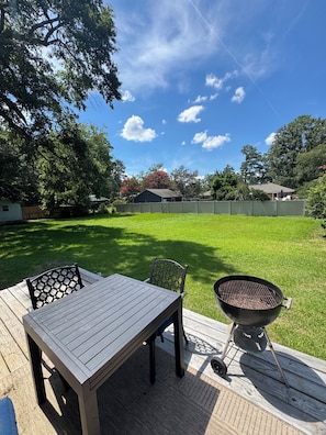 Un patio trasero con una terraza de madera, una mesa con sillas y una parrilla.