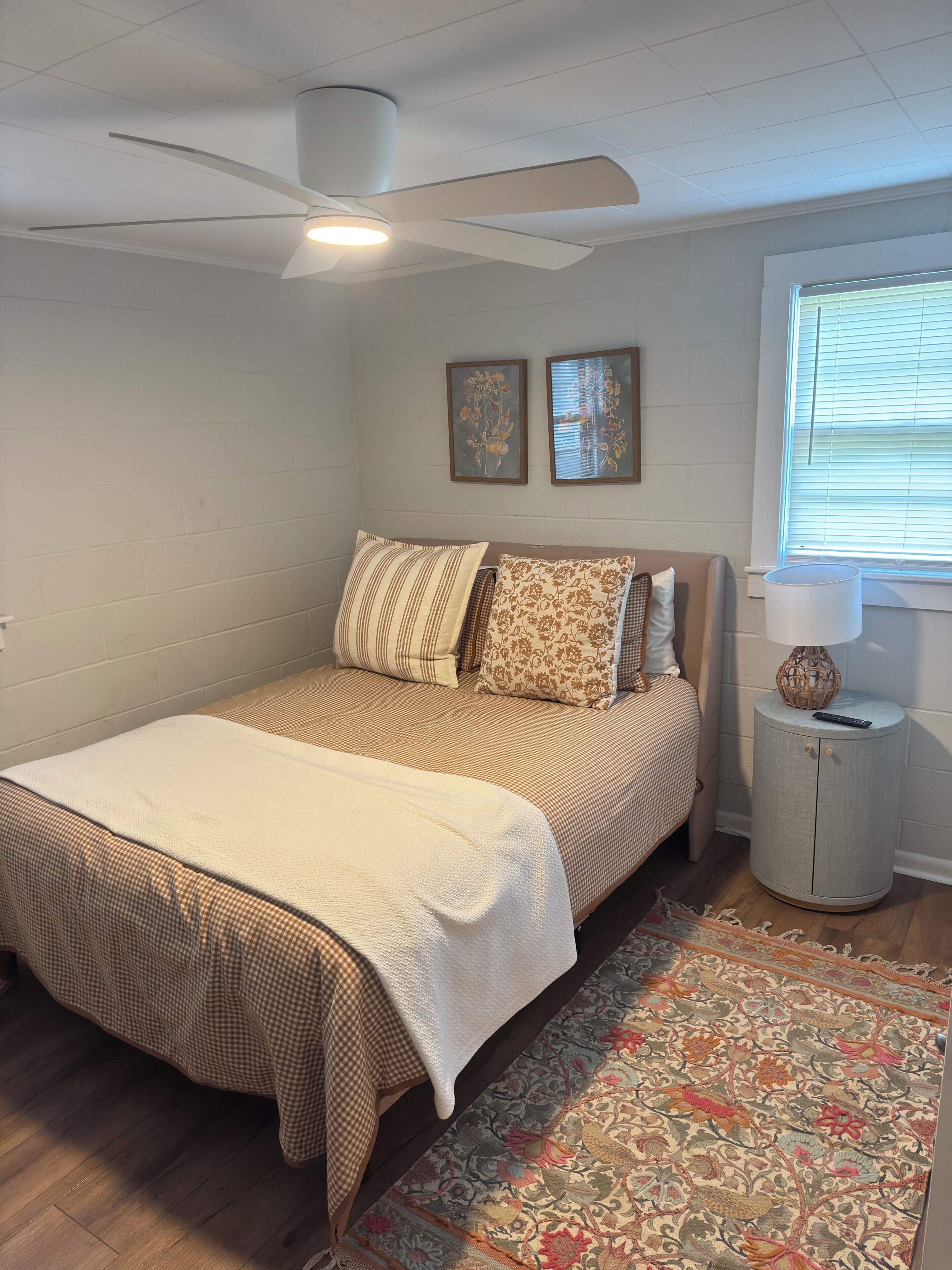 A bedroom with a bed, a ceiling fan, a window with blinds, a nightstand, and a rug.
