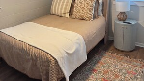 Quarto com cama, ventilador de teto, janela com persianas, mesa de cabeceira e tapete.