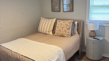 A bedroom with a bed, a ceiling fan, a window with blinds, a nightstand, and a rug.