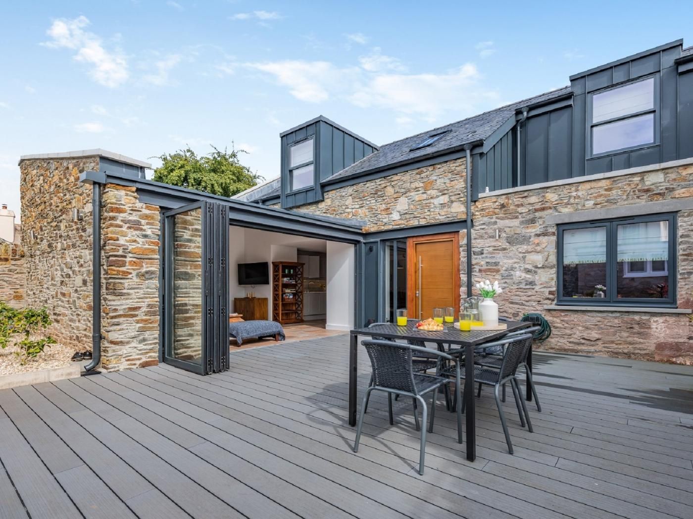 A modern house with a stone exterior, a deck with outdoor furniture, and a large window.
