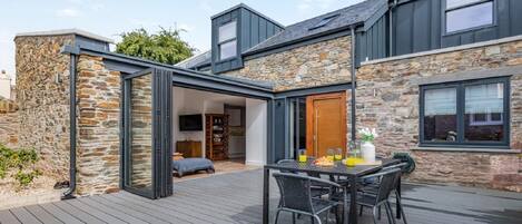 A modern house with a stone exterior, a deck with outdoor furniture, and a large window.