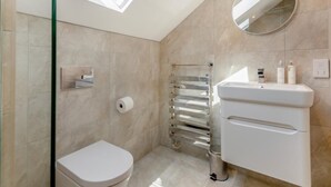 Ein modernes Badezimmer mit Oberlicht, Toilette, Duschkabine mit Glastür und Waschtisch mit Spiegel.