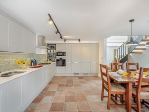 A modern kitchen with white cabinets, a dining table with chairs, and a staircase leading to an upper level. - 3 Bed in Brixham (oc-90614) (Brixham)